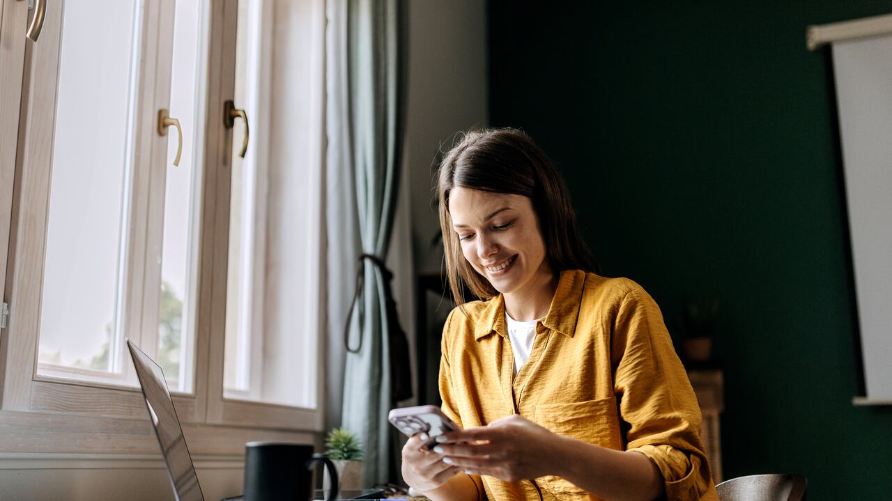 Young smiling woman text messaging while working at home office