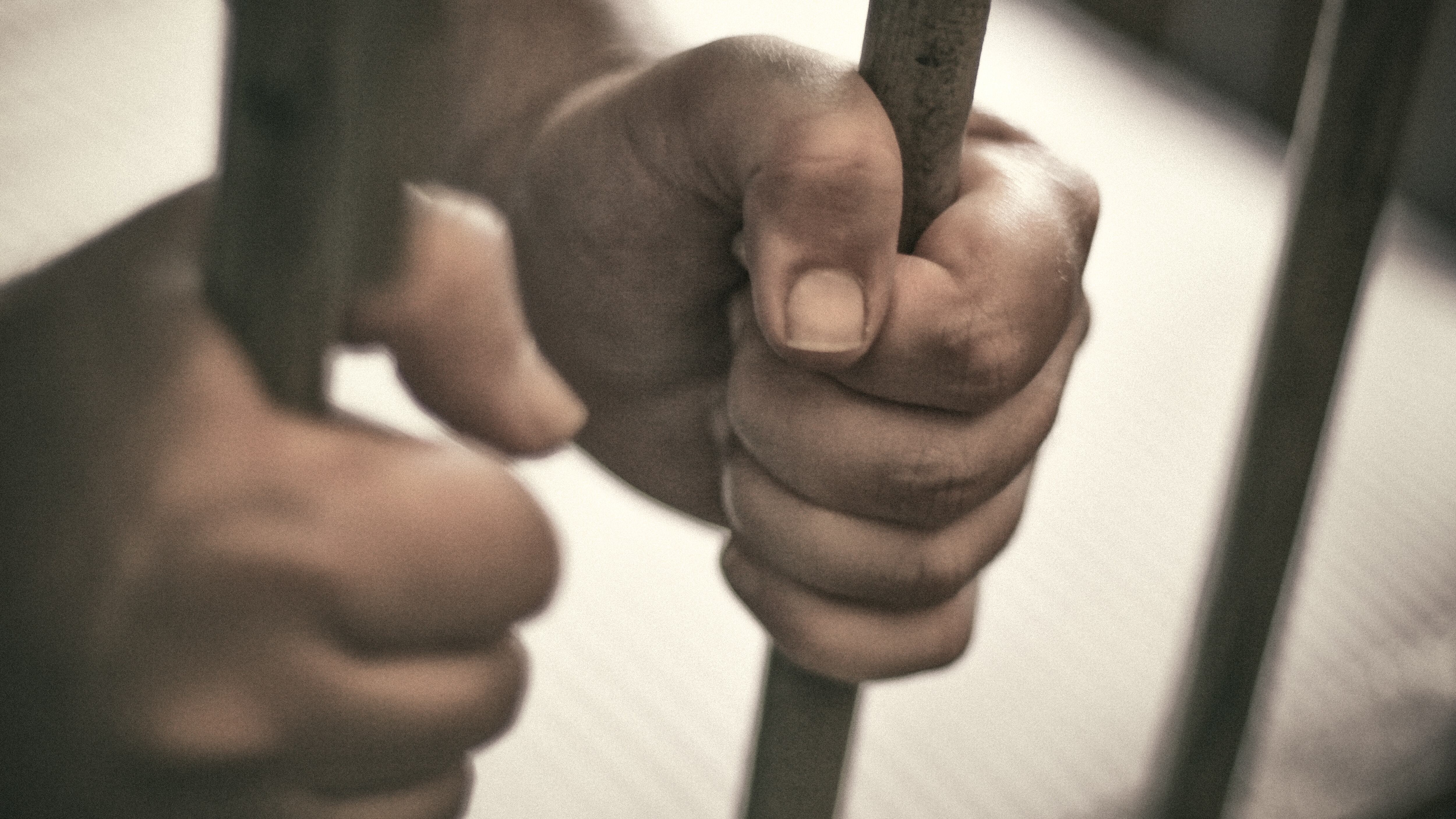 Las manos del hombre sujetan con fuerza los barrotes de su celda.