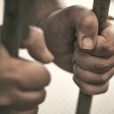 Las manos del hombre sujetan con fuerza los barrotes de su celda.