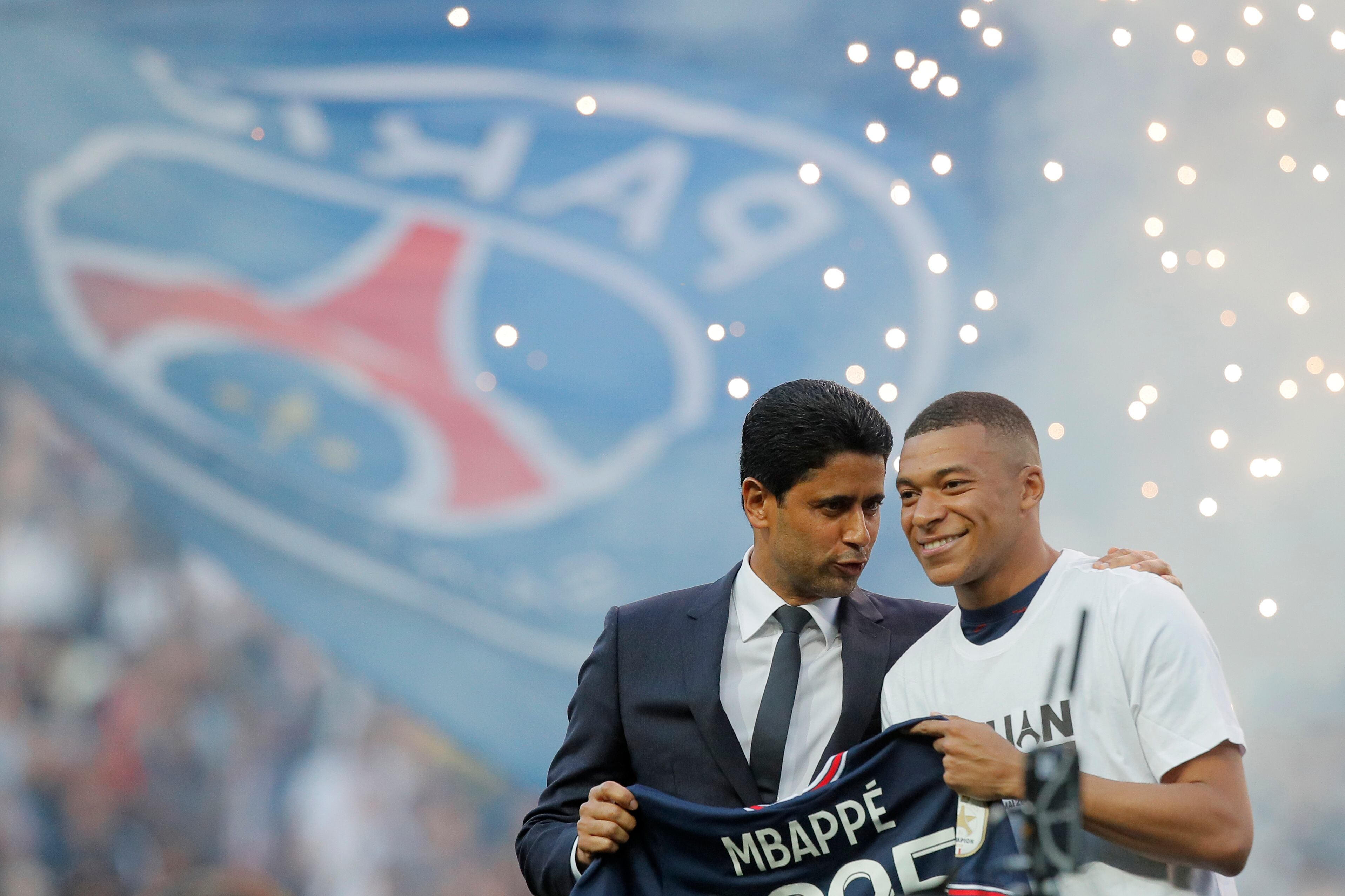 PSG President Nasser Al-Khelaifi, left, speaks to PSG's Kylian Mbappe who holds a shirt with his name and 2025 on it as it is announced he has signed a three year extension to his contract on the pitch ahead of the French League One soccer match between Paris Saint Germain and Metz at the Parc des Princes stadium in Paris, France, Saturday, May 21, 2022. (AP Photo/Michel Spingler)