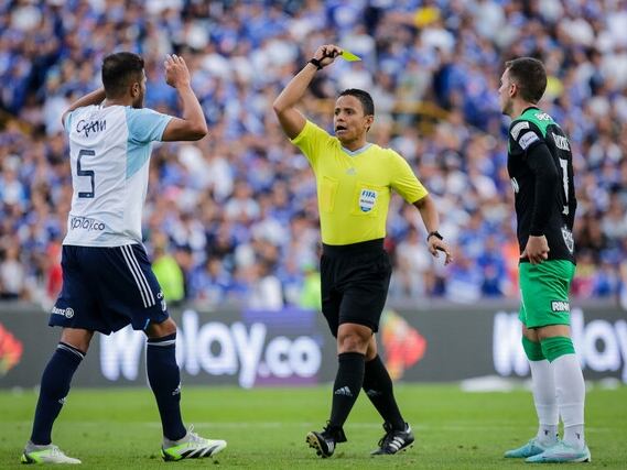 El arbitro Bismark Santiago le muestra la cartulina amarilla a Larry Vásquez en medio del clásico entre Millonarios y Nacional