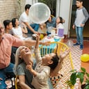 Felices padres mexicanos sentados con su nieto en sillas y jugando con un globo durante una celebración de cumpleaños en casa.