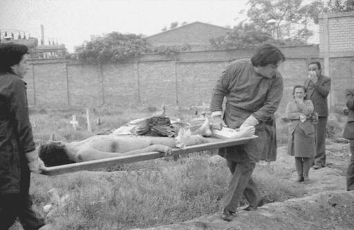 En esta fotografía se observan dos personajes transportando el cuerpo de un hombre. Se alcanza a ver que el cadáver no está descompuesto, lo que quiere decir que posiblemente no lleva mucho tiempo muerto. Llaman la atención varios orificios de bala en el hombro, el tórax y la pierna. El cuerpo presenta lo que se conoce como ‘tatuaje’, que básicamente son restos de pólvora que evidencian que los disparos pudieron ser a corta distancia. Se ven trozos de ropa ensangrentada sobre el cuerpo. En los registros oficiales de los cementerios de Bogotá no existe aviso alguno del entierro de un NN el 22 de enero de 1986, día que fue tomada esta foto