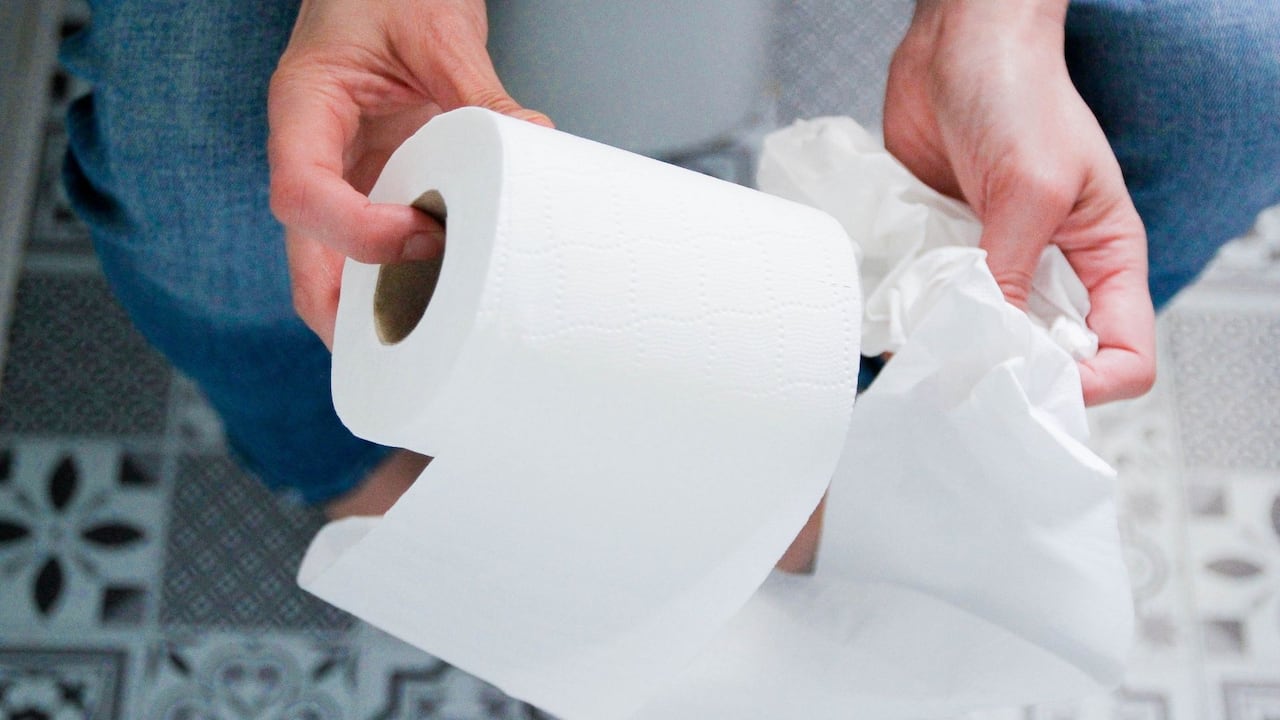 Persona en el baño sujetando un papel higiénico.
