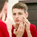 Cerca de un joven atractivo con piel problemática y cicatrices de acné se ve en el espejo del baño