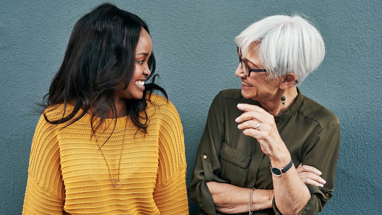 Foto de dos alegres mujeres de negocios discutiendo mientras están de pie contra una pared al aire libre