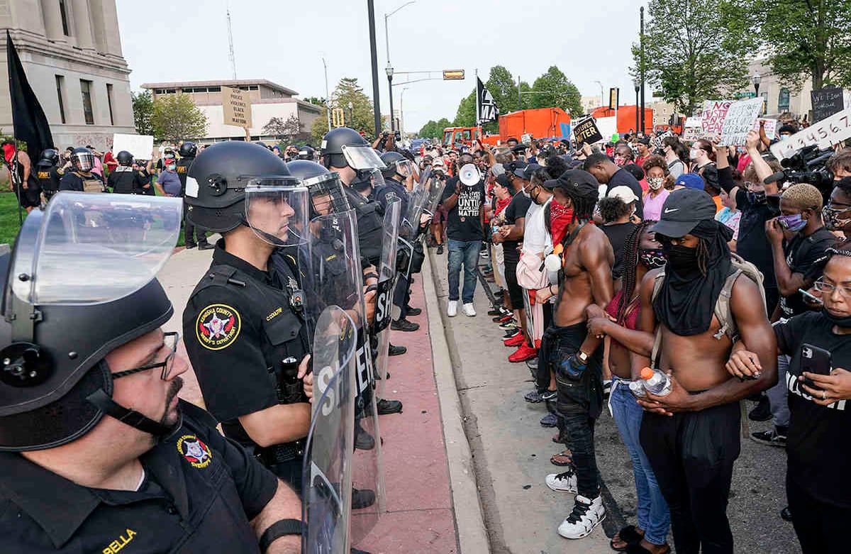 Los manifestantes enlazan los brazos frente a una línea policial frente al palacio de justicia del condado de Kenosha el lunes 24 de agosto de 2020 en Kenosha, Wisconsin. El gobernador de Wisconsin, Tony Evers, convocó a la Guardia Nacional para detener otra ronda de protestas violentas después del tiroteo de la policía. un hombre negro convirtió a Kenosha en la ciudad más reciente del país en un verano de disturbios raciales. Foto: Morry Gash / AP 