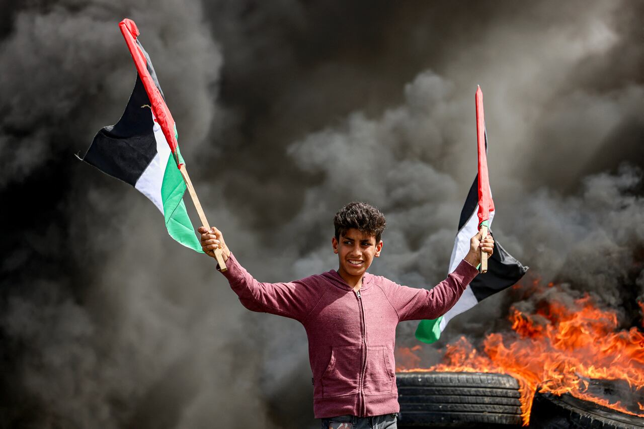 Un joven sostiene banderas palestinas junto a los gases de los neumáticos en llamas durante una manifestación a lo largo de la frontera con Israel al este de la ciudad de Gaza el 5 de abril de 2023.
(Foto de MAHMUD JAMONES / AFP)