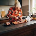 Skilled mid-adult woman, preparing vegetables and medium rare sirloin steak for the lunch in her modern kitchen while her mixed-breed/ponter dog makes her a company