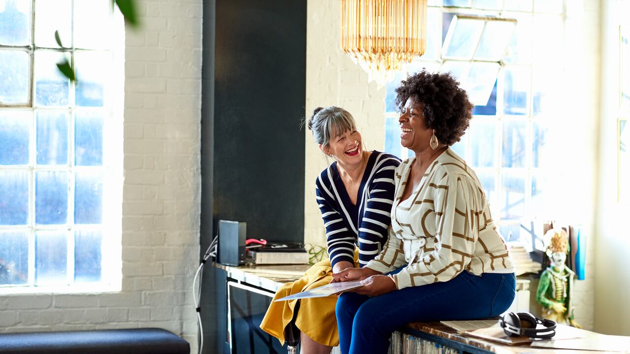 Two female friends sitting on sideboard and smiling, friendship, fun, memories, wellbeing