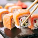 Chopstick holding Sushi Rolls Set with Salmon and Cream Cheese and Cuccumber on Black Slate Plate Close Up. Uramaki, Nori Maki or Futomaki Sushi with Trout Fillets, Soy Sauce and Wasabi