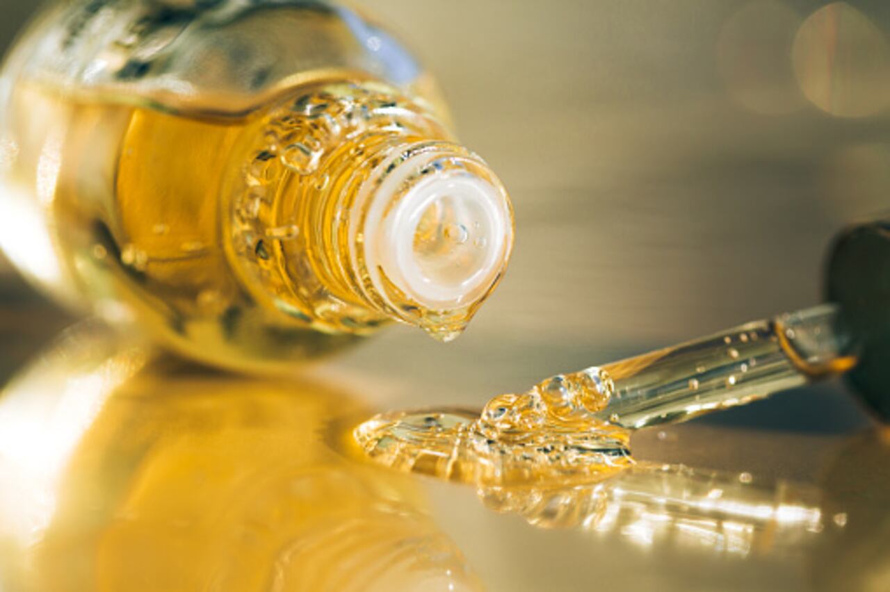 Drops of bright yellow essential oil with air bubbles are dripping from glass bottle and pipette on ultimate gray surface. Trendy colors of the year 2021. Extreme close-up and front view