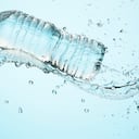 Gran salpicadura de agua limpia y refrescante con una botella de agua saludable en el estudio sobre un fondo azul claro para una vida saludable