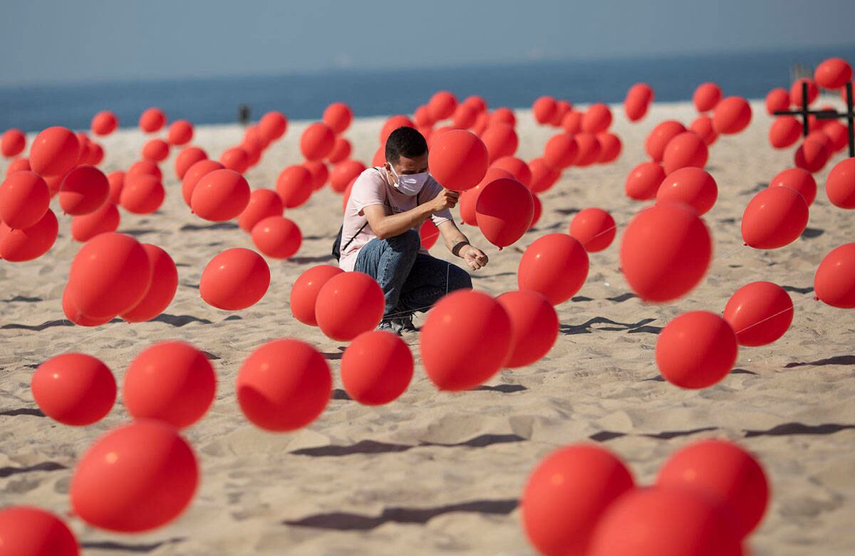 Un hombre ayuda a colocar globos rojos en la playa de Copacabana, Río de Janeiro, con motivo de una manifestación organizada por Río de Paz para honrar a las víctimas del covid-19 en Brasil. Este país se dirige a un hito de 100 mil nuevas muertes relacionadas con el coronavirus. Imagen del Sábado 8 de agosto. Foto: Silvia Izquierdo / AP