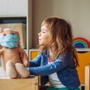 Niña jugando con peluche de conejo en la máscara de la medicina sentado en la mesa en la habitación de los niños.