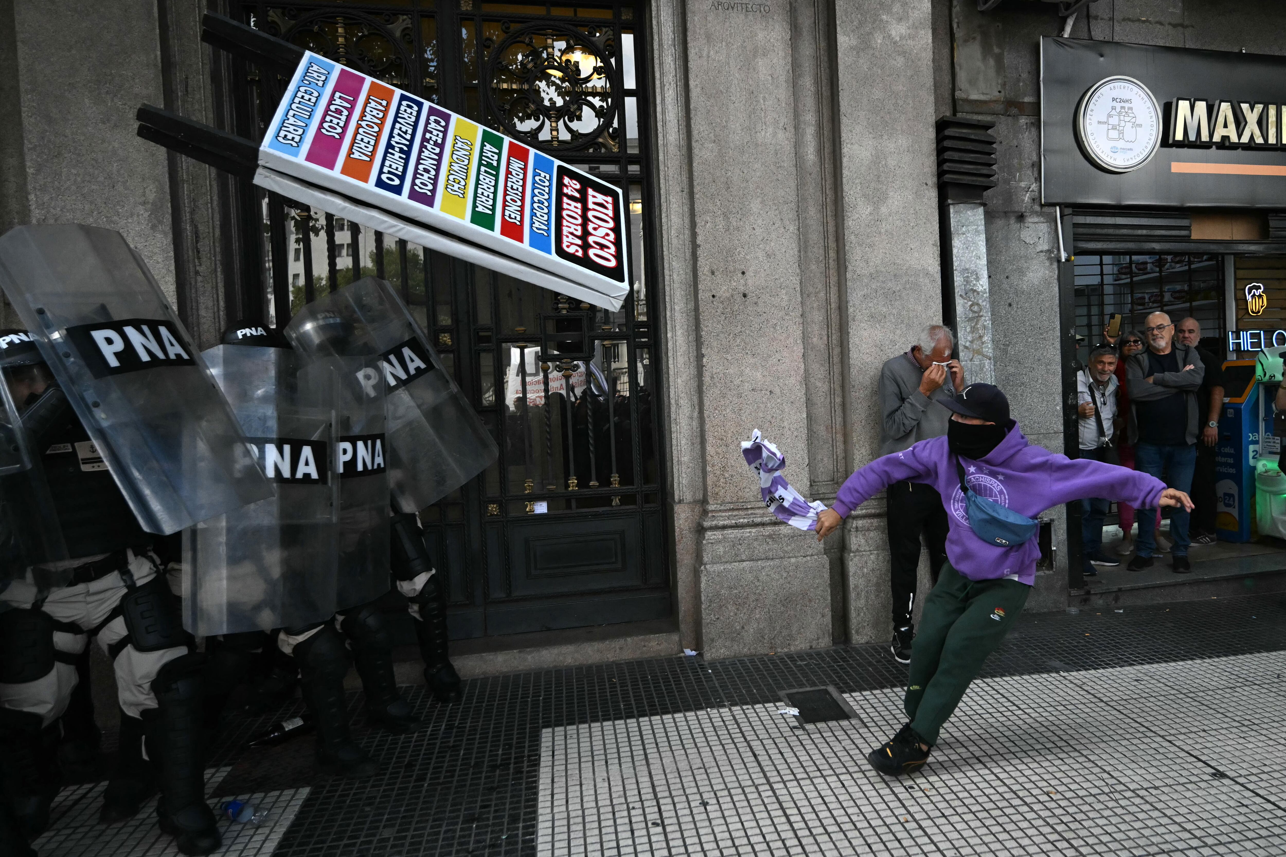 Un manifestante lanza una pancarta a la policía antidisturbios durante una protesta de jubilados.