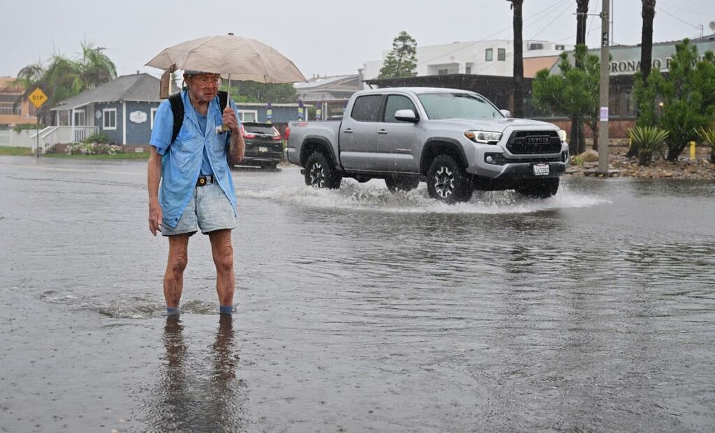 Patrick Brown sostiene su paraguas mientras cruza una intersección inundada en Imperial Beach, California, el 20 de agosto de 2023. El huracán Hilary se debilitó a tormenta tropical el 20 de agosto de 2023, mientras avanzaba por la costa del Pacífico de México, pero aún era probable para provocar inundaciones potencialmente mortales en el sudoeste de Estados Unidos, típicamente árido, dijeron los meteorólogos. Las autoridades reportaron al menos una muerte en el noroeste de México, donde Hilary azotó la península de Baja California con fuertes lluvias y fuertes vientos. (Photo by Frederic J. BROWN / AFP)