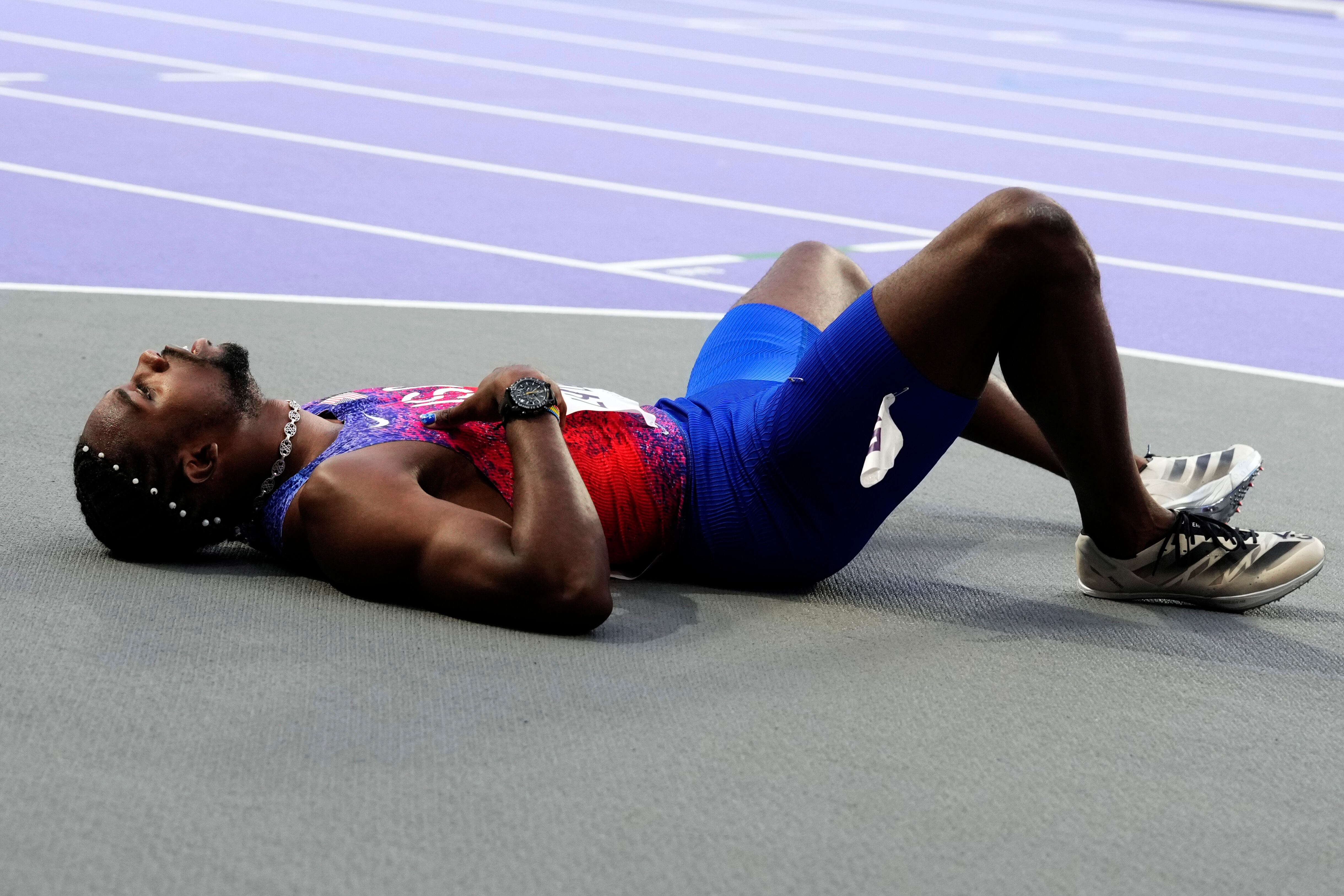 COVID-stricken Noah Lyles, of the United States, lies on the track after competing in the men's 200-meter final at the 2024 Summer Olympics, Thursday, Aug. 8, 2024, in Saint-Denis, France. Lyles said he tested positive for COVID two days before he finished third in the 200-meter final. (AP Photo/Petr David Josek)