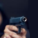 Mujer apuntando con un arma al objetivo en un fondo oscuro, enfoque selectivo en el arma frontal