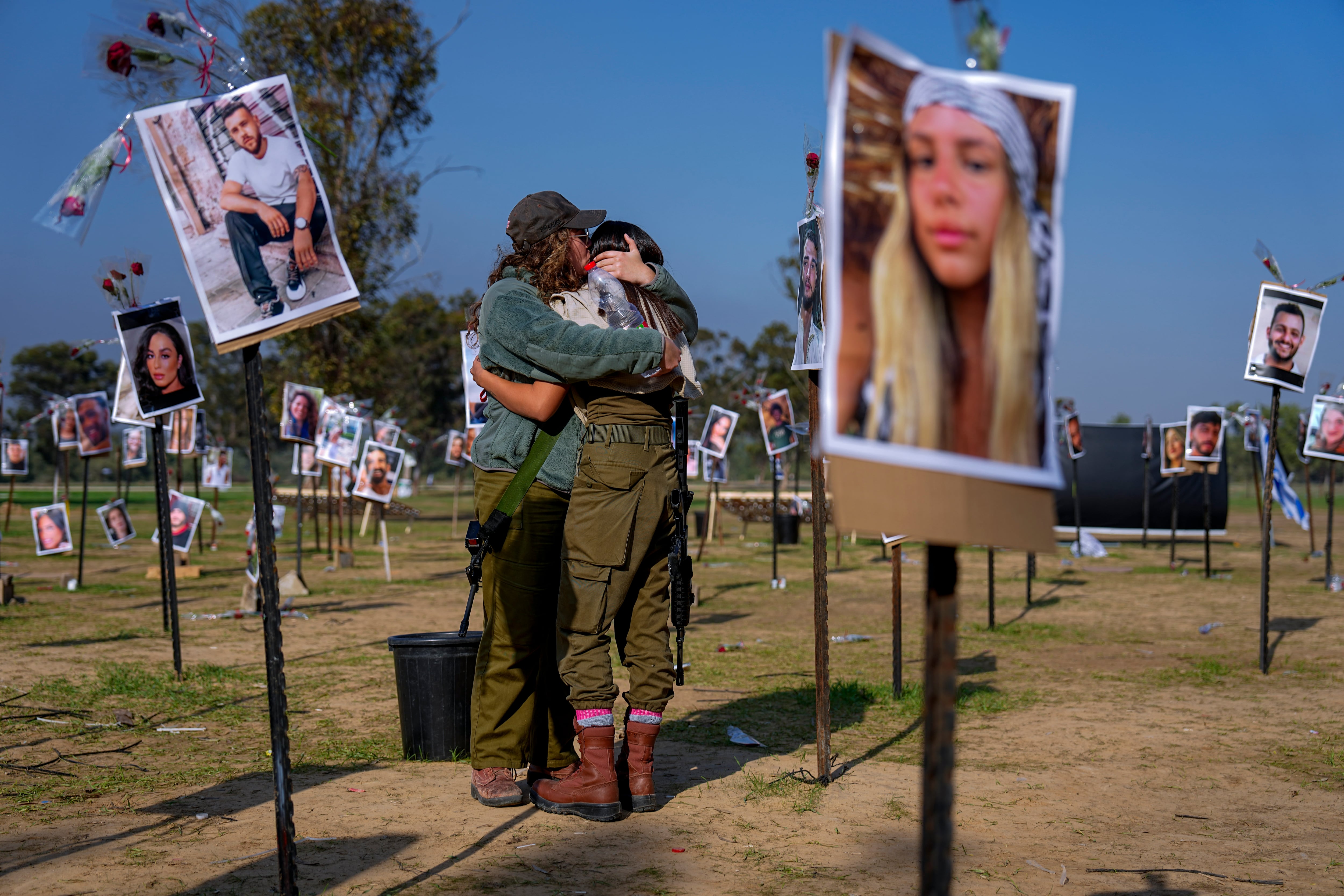 Soldados israelíes se abrazan junto a fotografías de personas asesinadas y tomadas cautivas por militantes de Hamas durante su violento ataque en el festival de música Nova en el sur de Israel