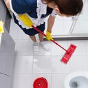 Ama de llaves o sirvienta con uniforme limpio y delantal de pie fregando el suelo en un baño visto desde arriba