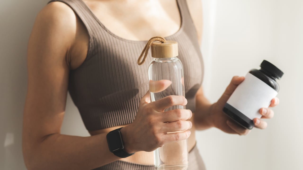 Mujer sosteniendo una botella de agua y una botella de vitaminas o proteínas. Concepto de estilo de vida saludable y deporte.