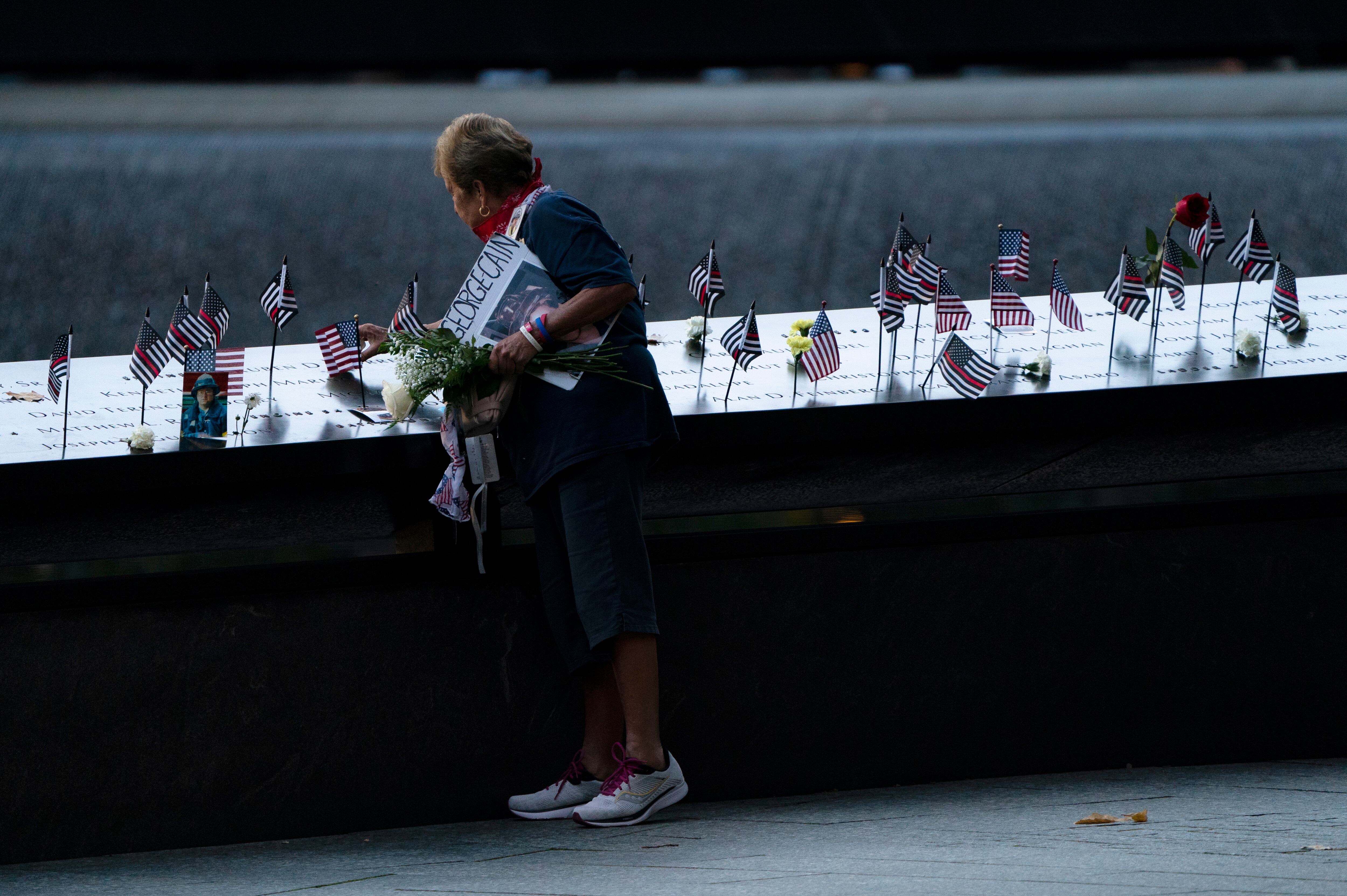 Una doliente coloca una bandera en la piscina sur antes de las ceremonias para conmemorar el vigésimo aniversario de los ataques terroristas del 11 de septiembre, el sábado 11 de septiembre de 2021, en el Museo y Memorial Nacional del 11 de septiembre en Nueva York. (Foto AP / John Minchillo)