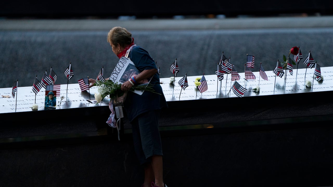 Una doliente coloca una bandera en la piscina sur antes de las ceremonias para conmemorar el vigésimo aniversario de los ataques terroristas del 11 de septiembre, el sábado 11 de septiembre de 2021, en el Museo y Memorial Nacional del 11 de septiembre en Nueva York. (Foto AP / John Minchillo)