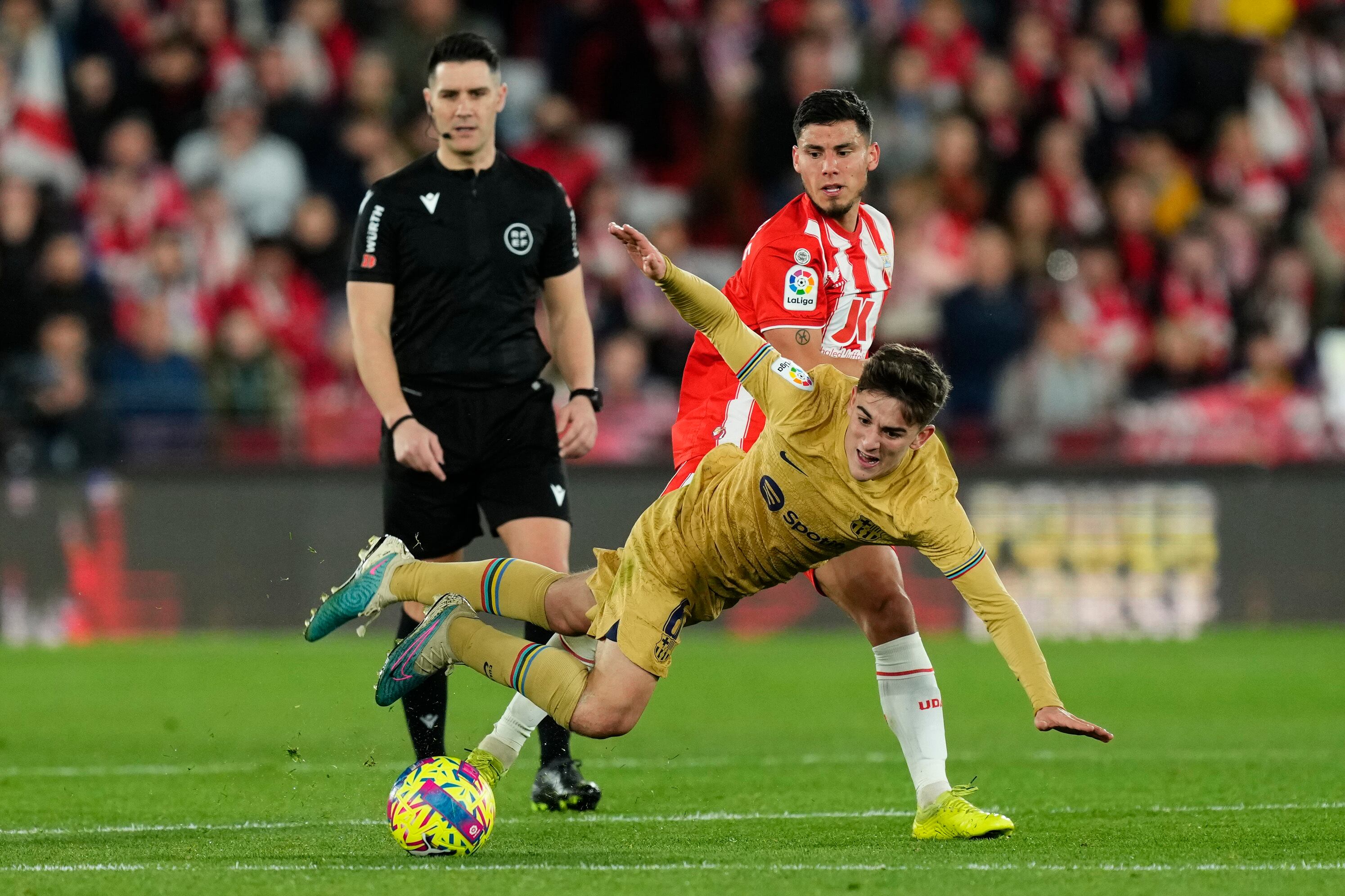 Barcelona's Gavi, right, falls next to Almeria's Lucas Robertone during the Spanish La Liga soccer match between Almeria and Barcelona at the Juegos Mediterraneos stadium in Almeria, Spain, Sunday, Feb. 26, 2023. Almeria won 1-0. (AP Photo/Jose Breton)