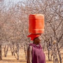 Namibia rural - 21 de agosto de 2016. Una mujer de Namibia regresa a su aldea sin agua, con un recipiente de plástico con agua potable en la cabeza, un ejemplo de los crecientes problemas de la falta de agua potable y los efectos del cambio climático.