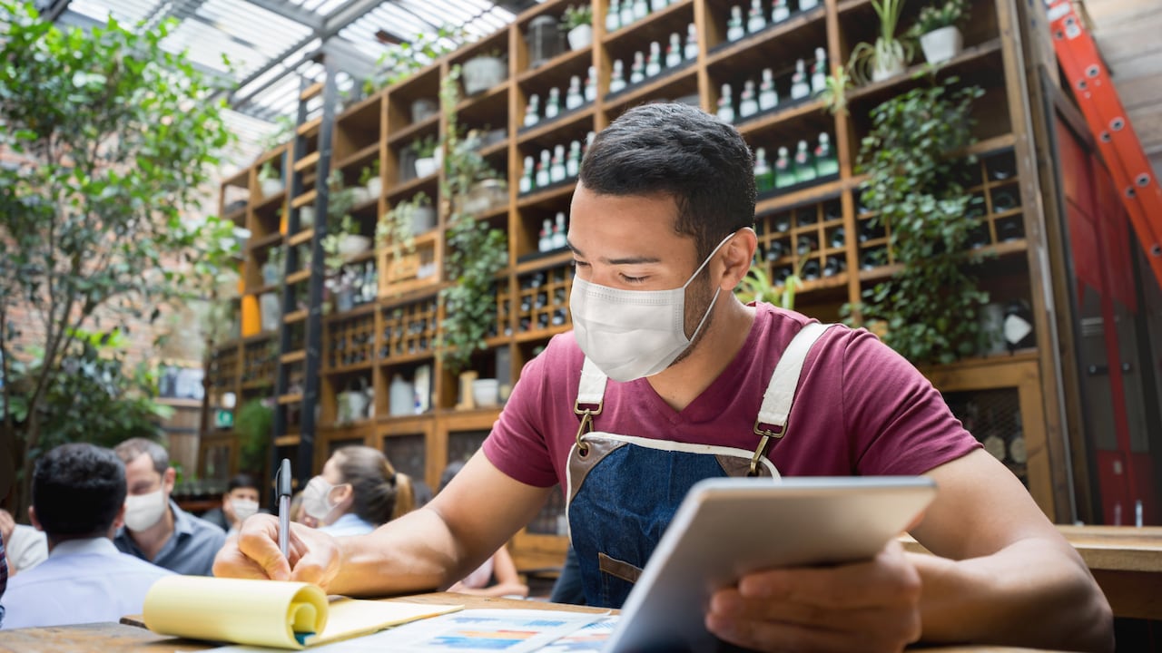 Retrato de un gerente de negocios haciendo los libros en un restaurante con una máscara facial durante la pandemia de COVID-19 - reapertura del negocio