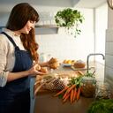 A woman smiles as she unpacks fresh organic vegetables from a plastic free bag in a zero waste kitchen.