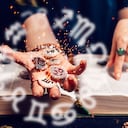Astrología y horóscopo. La mano de la adivina sostiene las brillantes piedras zodiacales en la palma de su mano sobre el libro abierto. El concepto de adivinación y magia. Foto: Getty Images.