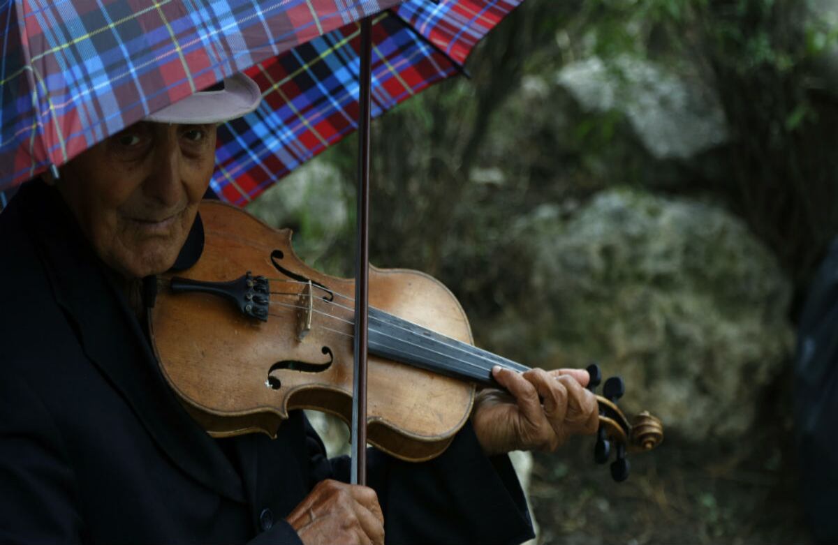 Un hombre toca el violín bajo una sombrilla mientras llueve en Belgrado, Serbia. (AP)