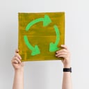 Un hombre irreconocible que sostiene un cartel en el aire con un símbolo de reciclaje. Es un activista que protesta por el cambio climático.