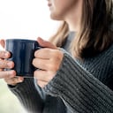 Retrato de una joven sonriente en suéter con taza de café. Ella toma café sentada cerca de la ventana, llueve afuera