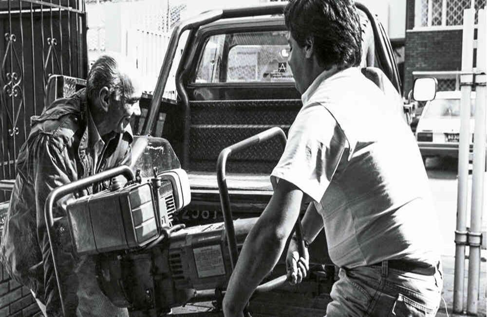 Dos hombres subiendo una motobomba durante la época del apagón en 1992. Foto: Lope Medina