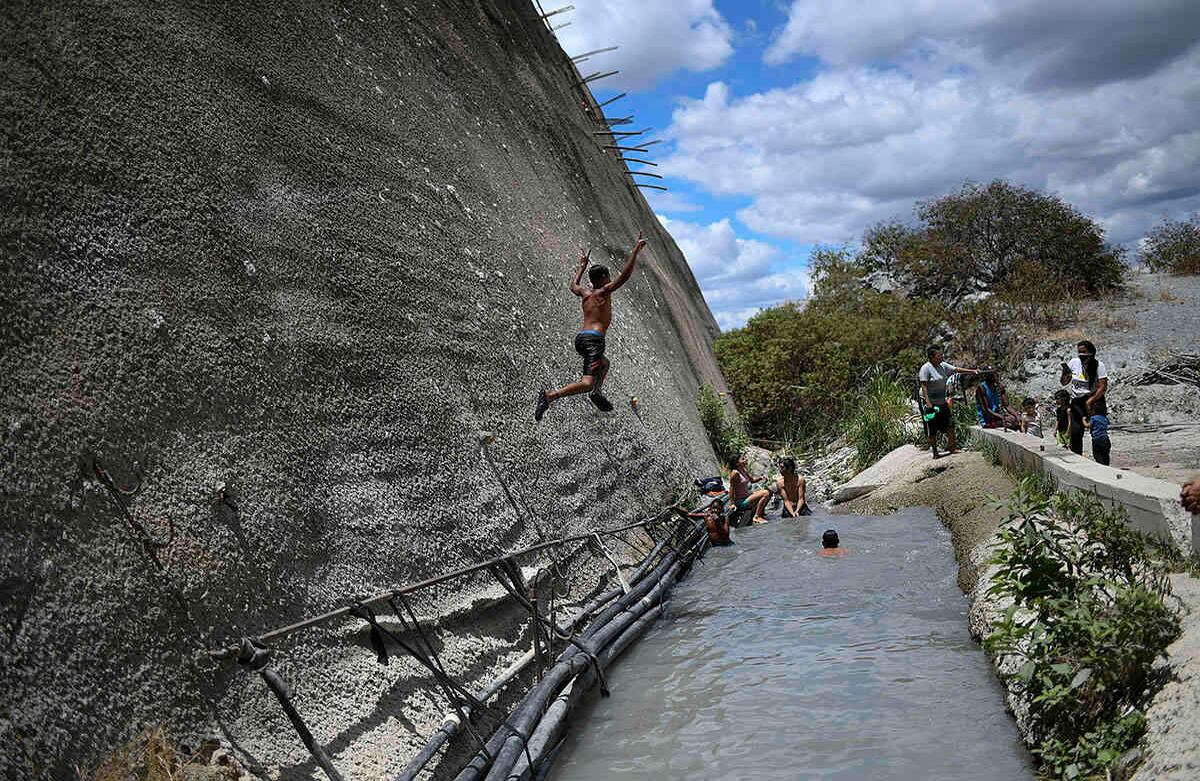  Un niño salta a una zanja que drena agua de un túnel de carretera abandonado en Caracas, Venezuela, el sábado 6 de junio de 2020. Para hacer frente a la escasez de agua, los residentes recurren a este lugar para bañarse y hasta consumir el líquido que sale del túnel. Foto: Matias Delacroix / AP.