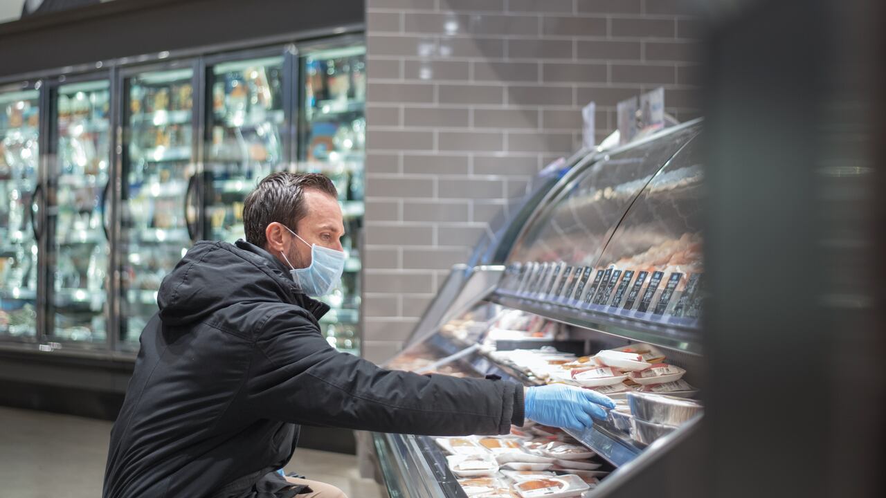 Un hombre usa mascarilla médica y guantes quirúrgicos en un esfuerzo por protegerse de contraer el coronavirus mientras compra en la tienda de comestibles