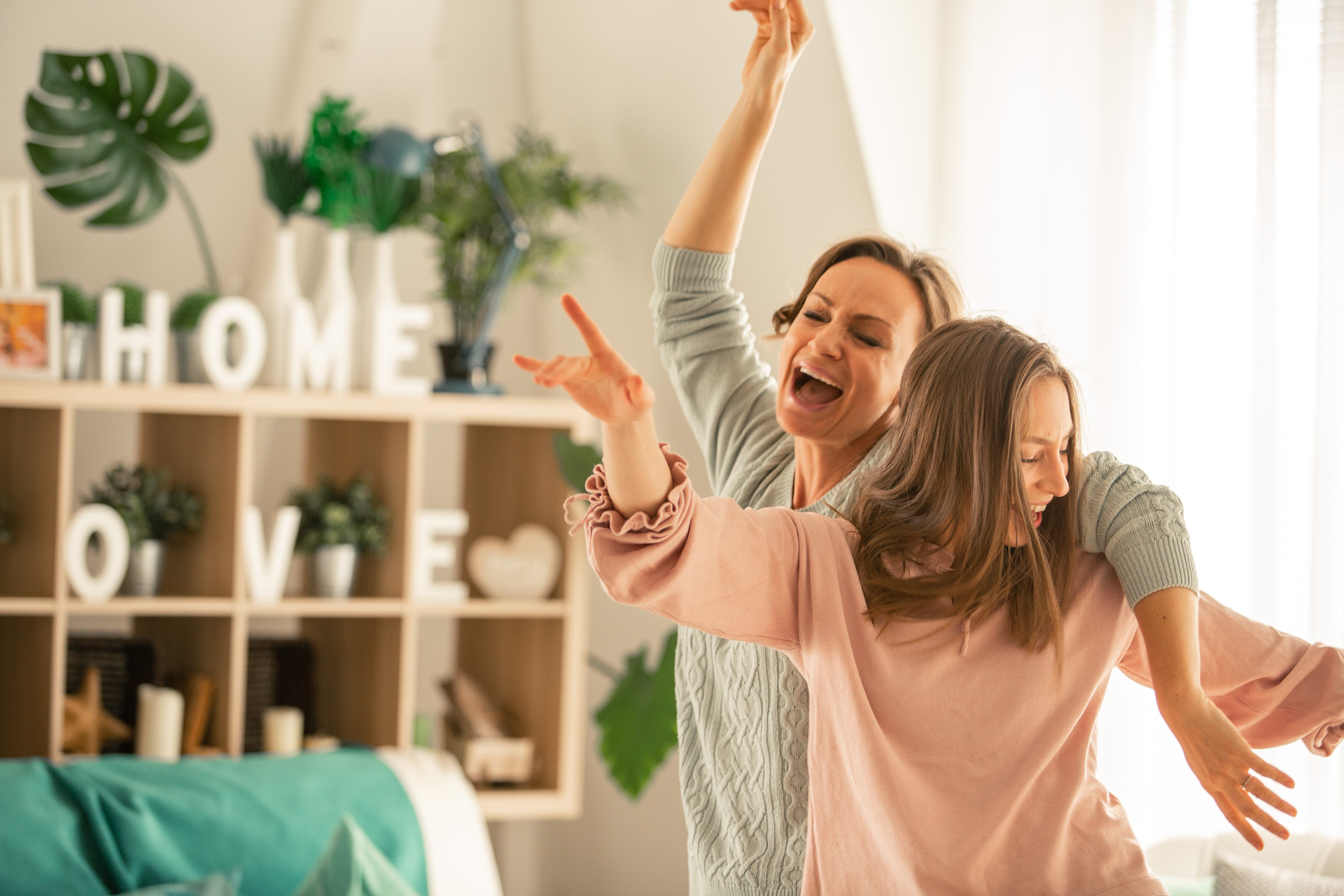 Mother and her daughter captured in the moment of pure joy and laughter while dancing and singing together in their living room.
