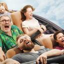 Momento de la vida, cosas más locas. Gente emocional en la montaña rusa bajando con prados en el fondo. Los hombres y mujeres caucásicos obtienen actividad de adrenalina y se divierten juntos en los paseos.