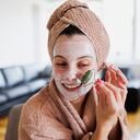 Woman using jade roller on her face at home. Young girl massaging face by jade roller. Self-care facial massage, anti-aging lifting skincare procedure