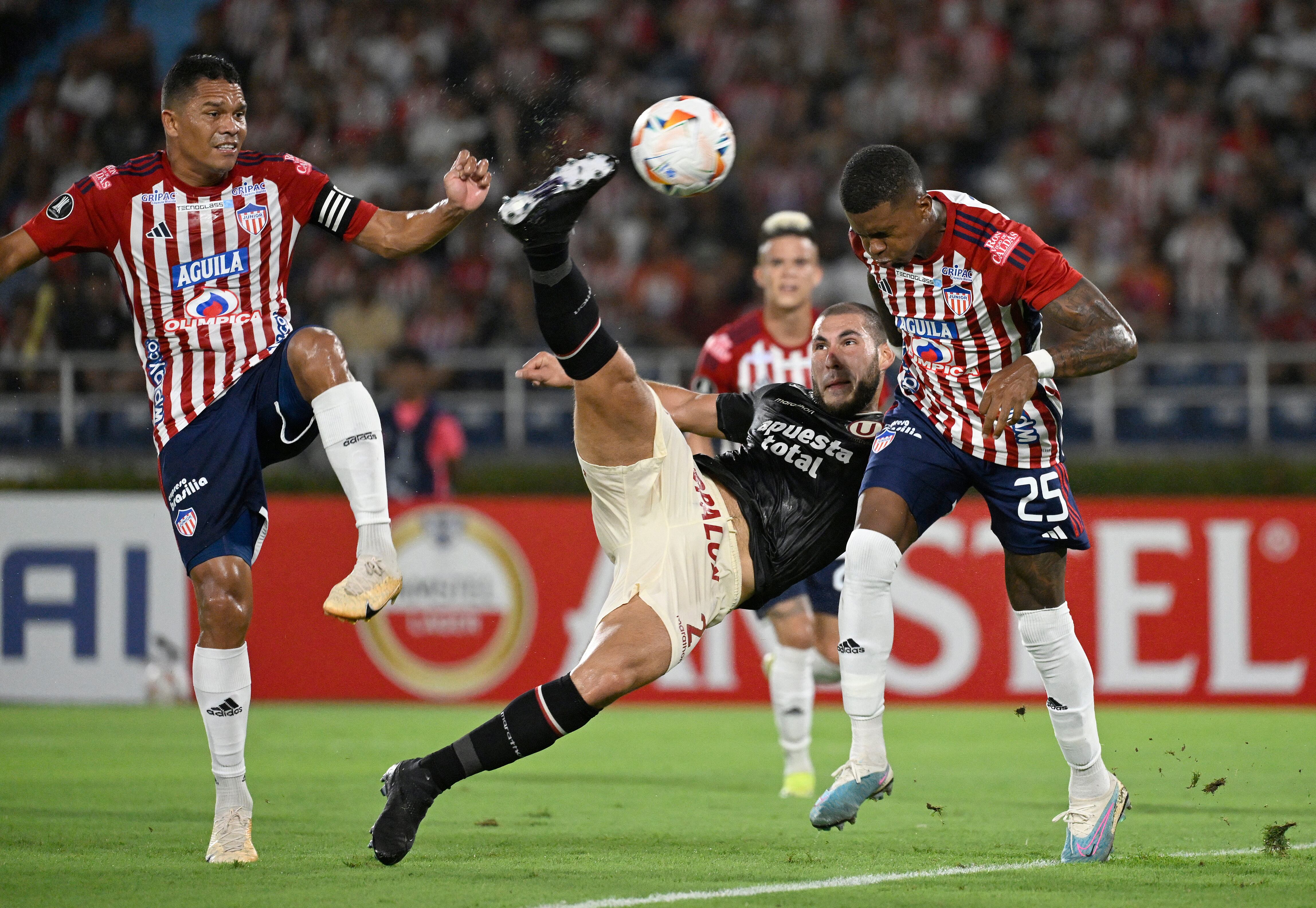 El defensa de Universitario Marcos Saravia (C) patea el balón entre el delantero de Junior Carlos Bacca (L) y el centrocampista Carlos Cantillo durante el partido de fútbol de ida de la fase de grupos de la Copa Libertadores entre Junior de Colombia y Universitario de Perú en el estadio Metropolitano Roberto Meléndez de Barranquilla.