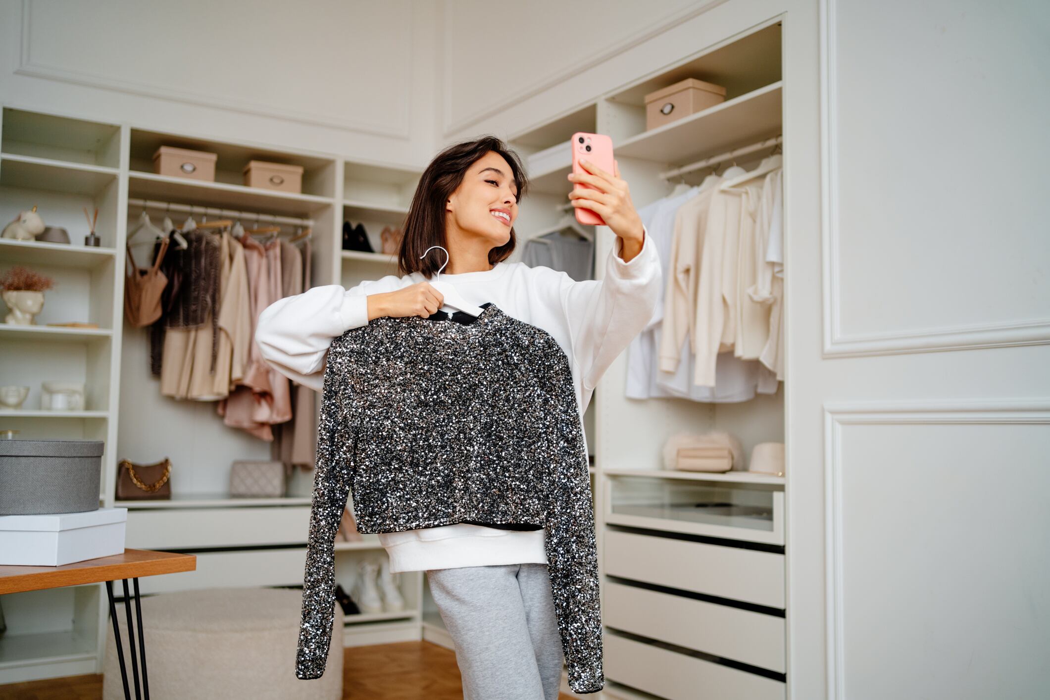 Brunette woman with clothes hanging taking selfies and holding new trendy jacket