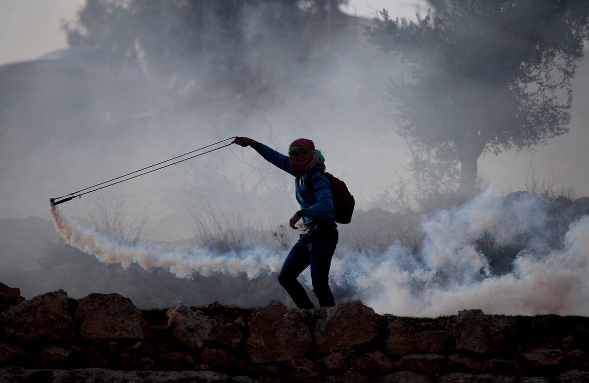 Un palestino usa una resortera para devolver un cilindro de gas lacrimógeno disparado por tropas israelíes, durante un enfrentamiento en las afueras de la prisión militar de Ofer, en Ramallah. (AP)