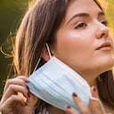 Primer plano de la cara de una mujer joven quitándose una mascarilla facial desechable que usa para evitar la propagación de una enfermedad viral.