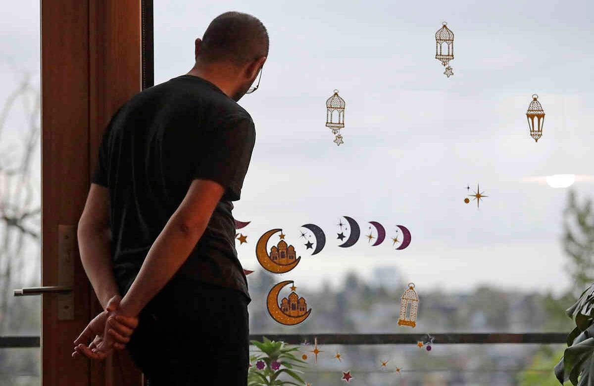 Ahmad Kamel mira hacia el oeste, esperando la puesta de sol mientras las pegatinas de Ramadán decoran la ventana junto a él, mientras espera junto con su familia para romper el Ramadán todos los días en su hogar familiar en medio del brote de coronavirus. La familia, como la mayoría de los musulmanes durante la pandemia en curso, está celebrando el mes de Ramadán de ayuno desde el amanecer hasta el atardecer, la oración y la reflexión desde su hogar, en lugar de en reuniones comunitarias y mezquitas. AP-Elaine Thompson