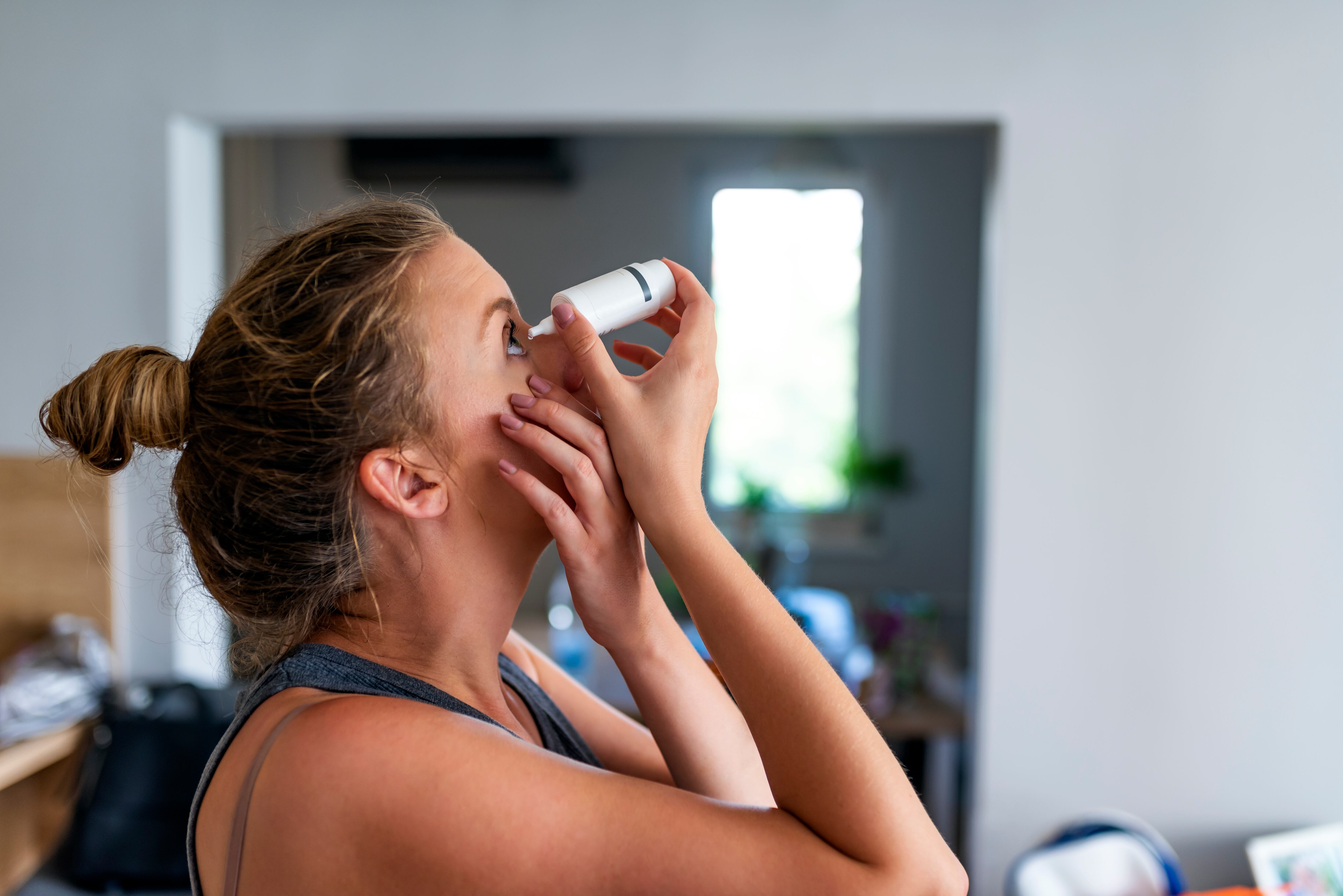 Photo of a woman using eye drop. Female dropping eye lubricant to treat dry eye or allergy. Sick girl treating eyeball irritation or inflammation; sick woman suffering from irritated eye, optical symptoms.