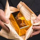 Businessman with gold bar wrapped in newspaper, like fish and chips.