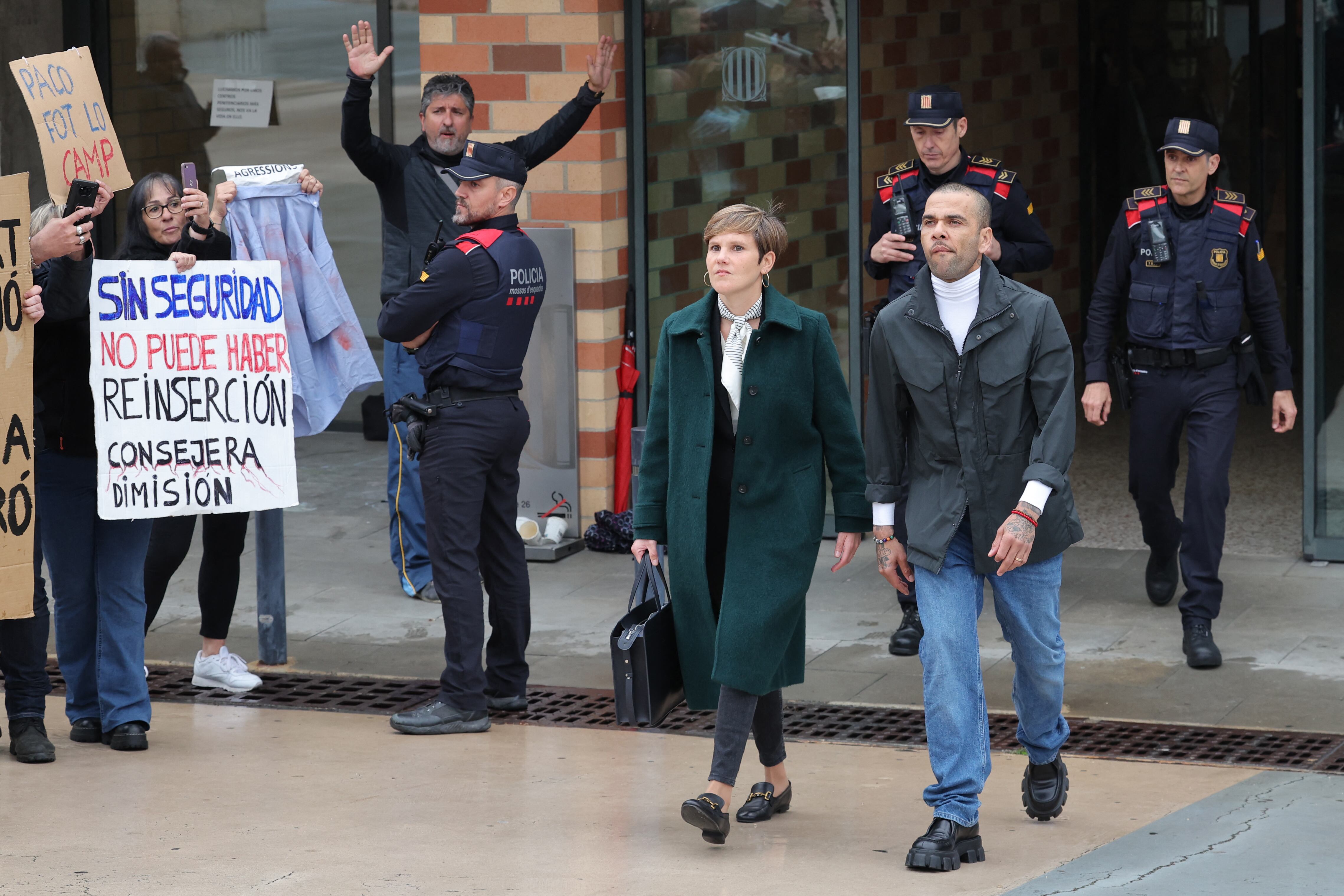 Prison workers unions' members protest over the killing of a cook by an inmate the week before, as convicted rapist and former Brazil international football player Dani Alves (R), flanked by his lawyer Ines Guardiola, leaves Brians 2 prison in San Esteban Sasroviras, near Barcelona, on March 25, 2024. Convicted rapist and former Brazil international Dani Alves left a jail in Barcelona on March 25, 2024 after posting the one-million-euro bail set by a Barcelona court to ensure his release pending appeal. Ex-Brazil star has been sentenced to 4.5 years in jail for rape on February 22, 2024. (Photo by LLUIS GENE / AFP)
